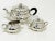 A silver tea set with a teapot, sugar bowl and a milk jug in an oval shape with a scalloped pattern and is lightly...