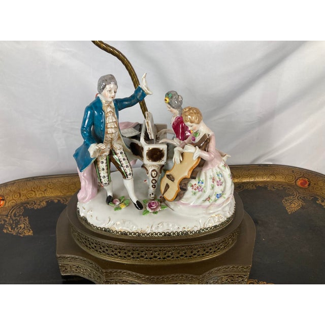 A porcelain figural group of three musicians, mounted as a table lamp. A gentleman in a teal coat and patterned breeches...