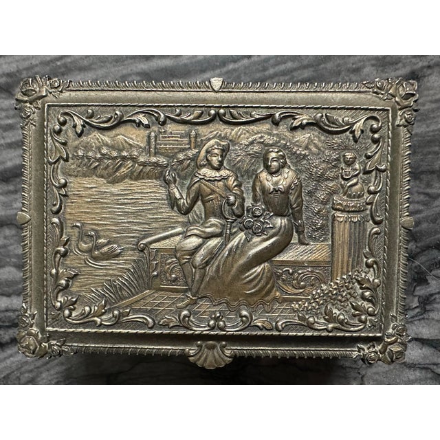 Vintage silver colored trinket/jewelry box with ornate Baroque-style floral scrollwork and detailed relief carvings. It is...