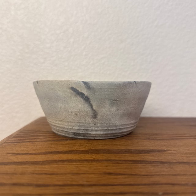 A rustic, small ceramic bowl handmade from clay with a matte, stone-gray finish. The piece features a marbled effect...