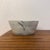 A rustic, small ceramic bowl handmade from clay with a matte, stone-gray finish. The piece features a marbled effect...