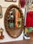 Elegant oval wall mirror featuring an ornate raised floral and foliate frame with a richly aged gilt finish. Its intricate...