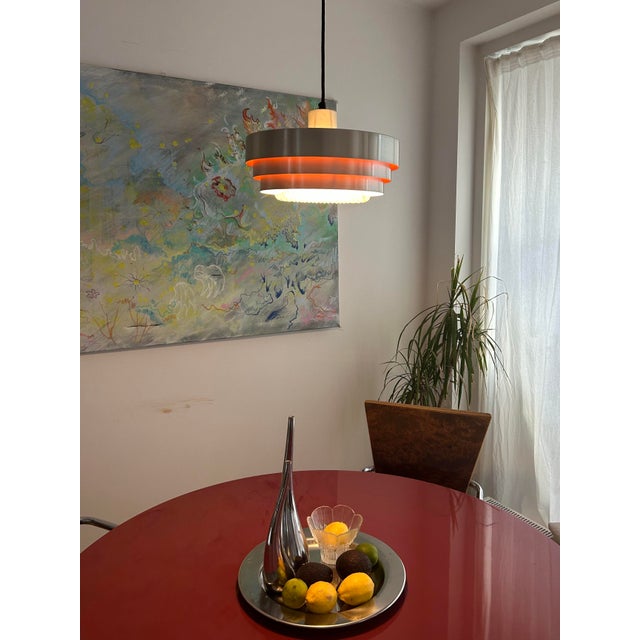 When lit, a warm orange glow spills out from between the nested aluminium bands, scattering across the bubbled glass...
