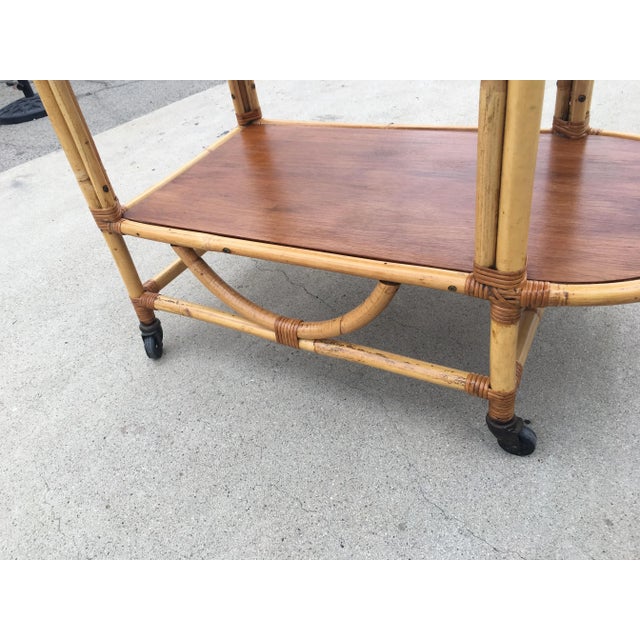Unique 1950s bar cart features a u-shaped frame with two tombstone shaped shelves in mahogany and metal ball wheels.