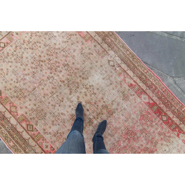 A distressed, hand-knotted Chinese Khotan rug featuring an overall floral motif. Features a mixture of colors using red as...