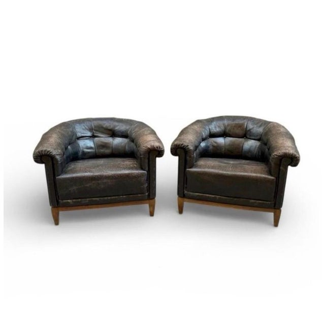 French Chesterfield-style club chairs, circa 1940, upholstered in black leather with button tufting and a low, curved...