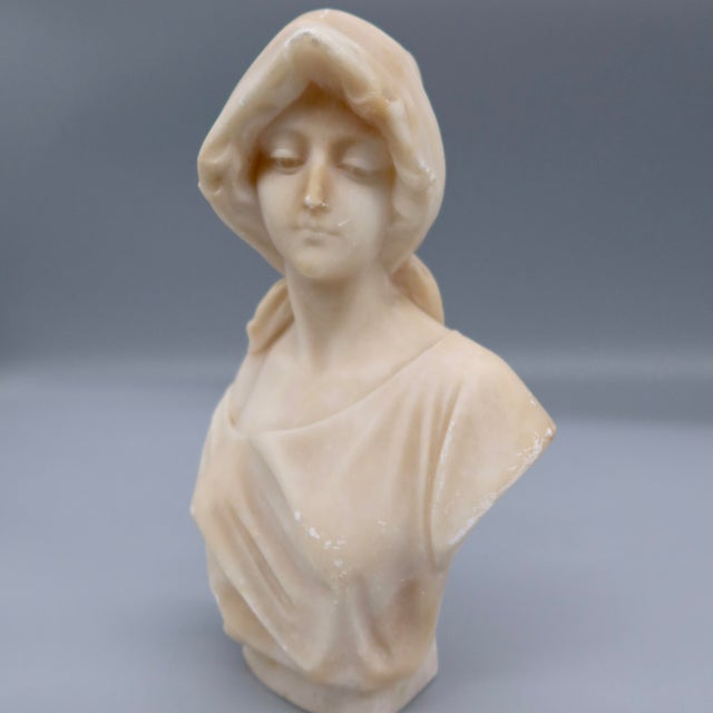 A beautifully carved alabaster bust of a young woman wearing a draped hood tied at the back of the head, attributed to the...