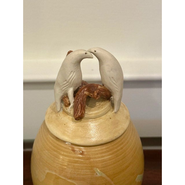 Two white birds sitting on top a piece of driftwood adorn the lid of this sweet piece of pottery. The main coloring is...