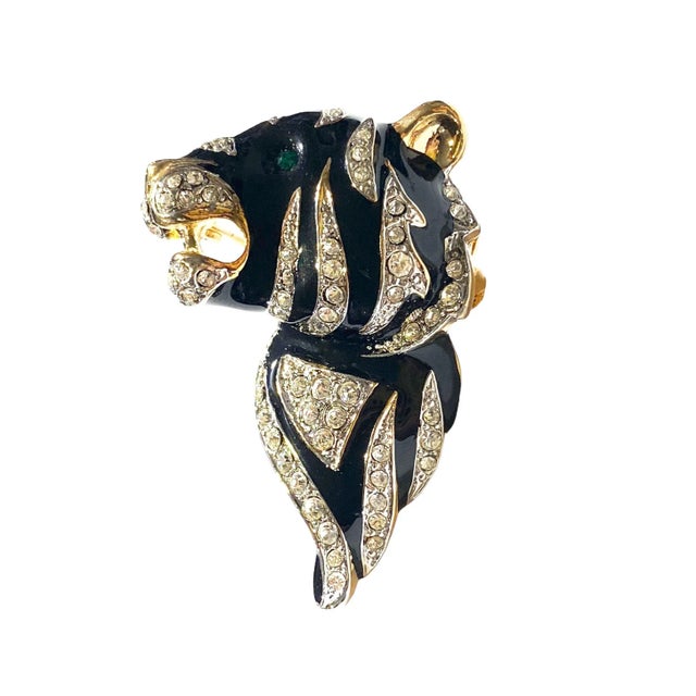 Elegant brooch pin features a sleek gold tone with black enamel and sparkling rhinestones, highlighted by a green emerald...