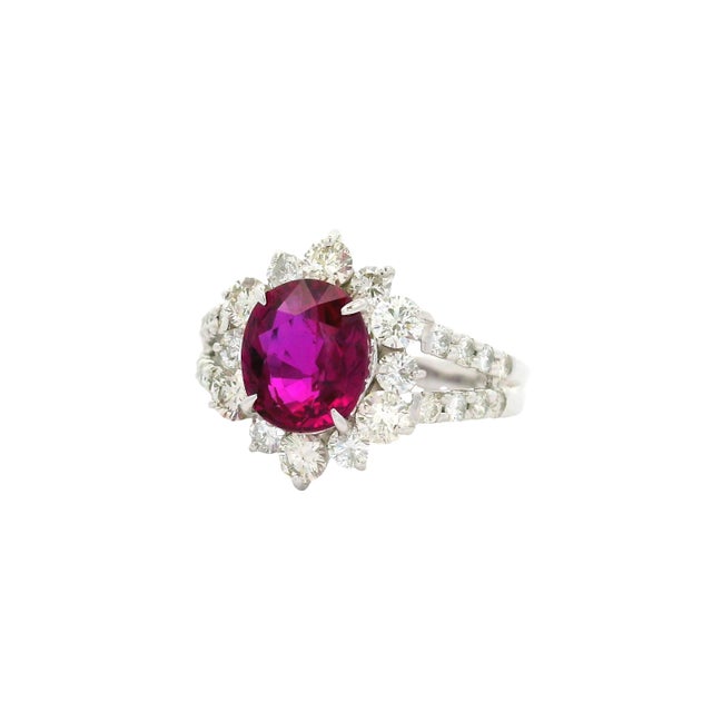 This contemporary piece features a striking 2.13-carat oval ruby at its center, radiating a deep red hue. Surrounding the...