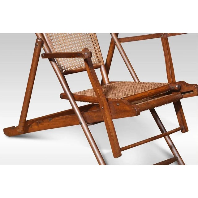 Walnut framed folding Steamer deck chair. The cane work back and seat, flanked by scrolling arms and splayed legs. It...