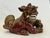 The glazed ceramic foo dog is portrayed crouching, with one paw resting and one on a ball. The back legs are relaxed and...