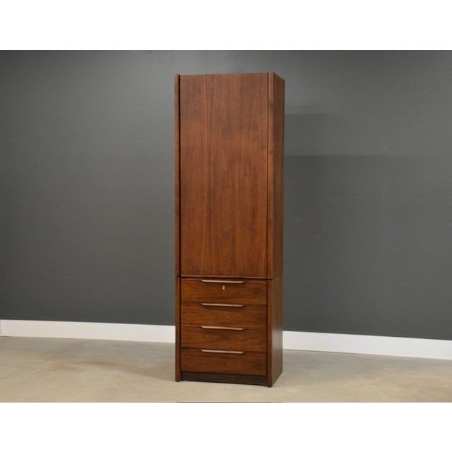 A mid century modern walnut tall dresser armoire with one large door, adjustable shelving and lower drawers made by...