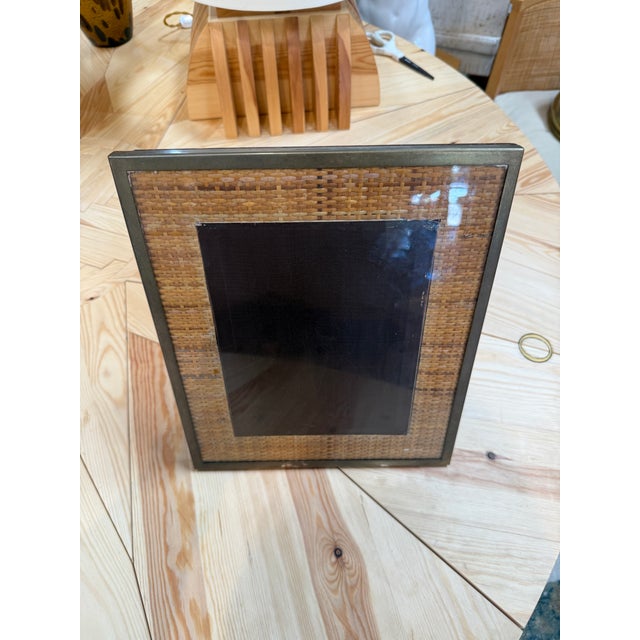 A rectangular picture frame with a warm woven rattan surround and a slim metal border. The natural texture gives it a...