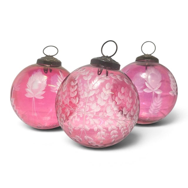 Three oversized cranberry glass ornaments create a luminous holiday grouping, each sphere carrying its own delicate...