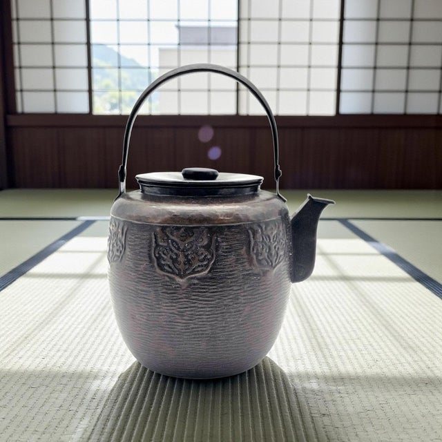 This vintage Japanese-style cast metal teapot presents a sculptural form distinguished by its hammered surface and a...