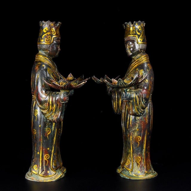 A striking pair of Chinese bronze figural sculptures, likely used as lamp holders or candle stands. Each figure depicts a...