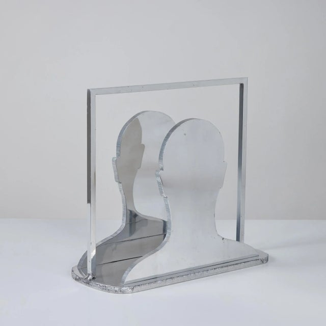 Aluminum silhouette magazine rack signed "M Tearney". The rack features a square frame with mirroring images of a smooth...