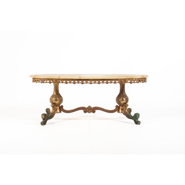 A striking vintage Hollywood Regency coffee table featuring an elegant natural onyx top resting on an ornate brass base....