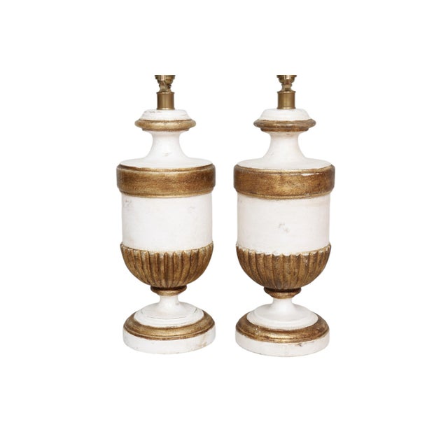 A pair of Hollywood Regency style table lamps by Visual Comfort. White painted urns are decorated with beveled shoulders...