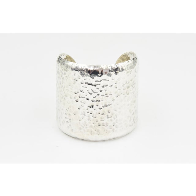 A striking cuff bracelet crafted from sterling silver. The surface features a hammered texture, creating a dynamic play of...