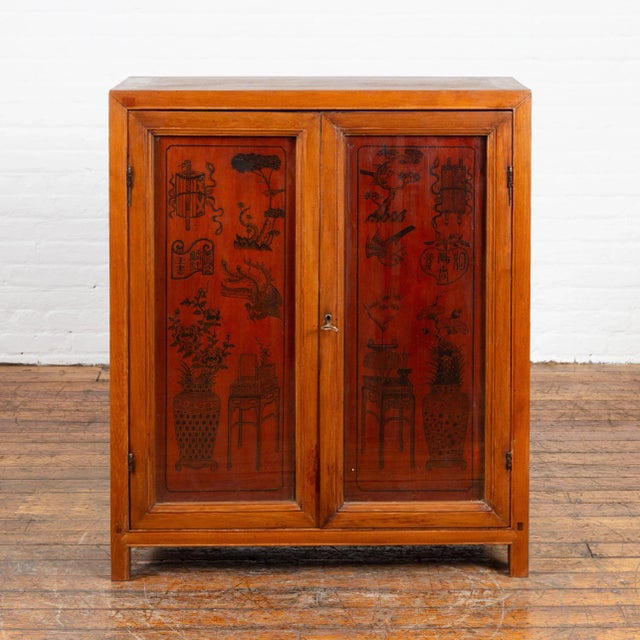An antique Chinese cabinet from the early 20th century, with ink decorated panels behind glass doors. Created in China...