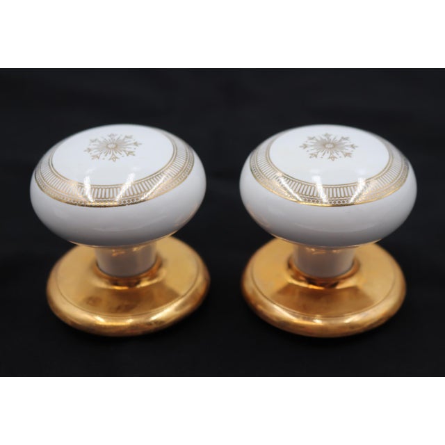 This vintage dummy door knob set includes two white ceramic door knobs with a gold snowflake motif and two polished brass...