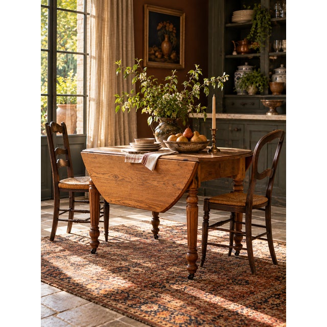 An antique drop-leaf dining table featuring beautifully grained wood, turned and fluted legs, and original casters. The...