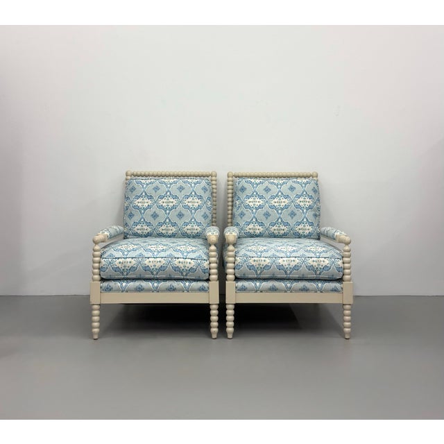 A stylish pair of contemporary lounge chairs featuring sculptural bobbin-turned frames finished in a soft ivory lacquer....