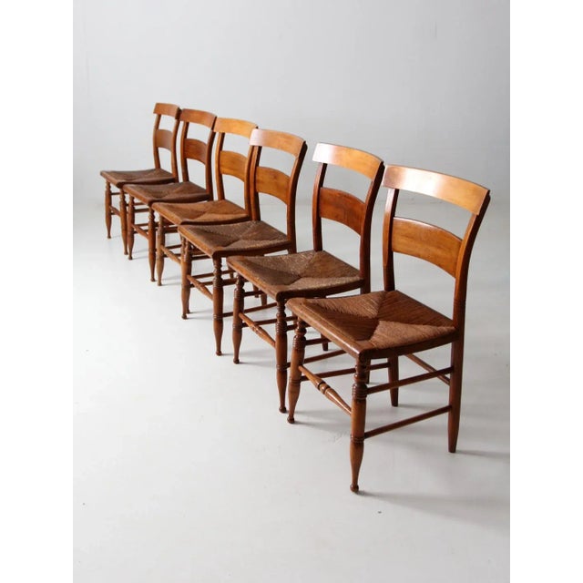 An exceptional set of six antique French farmhouse dining chairs featuring turned legs, textured rush seats, and a warm...
