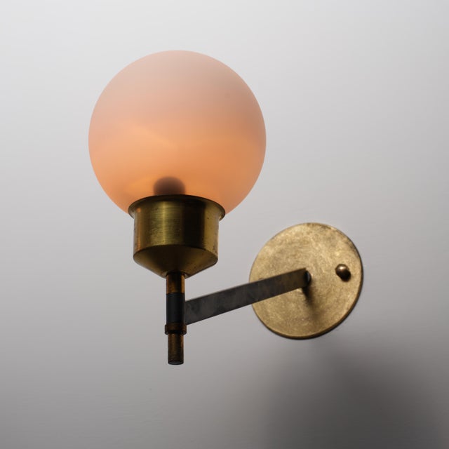 Pair of Italian wall sconces made in the 1950s, featuring a combination of brass, black-painted steel and opaline glass....