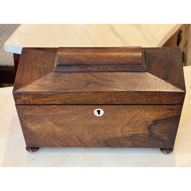 Rosewood tea caddy with a molded lid and bun feet. The interior includes two lidded compartments and a central section...