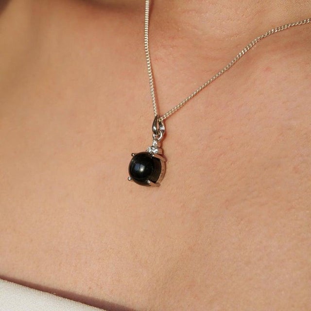 Crafted in 925 sterling silver, this elegant pendant features a mesmerizing 11.55 carat Black Star gemstone in a timeless...