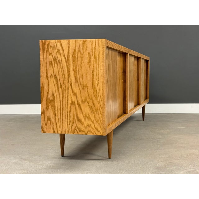 A mid century modern oak sliding door credenza with inset pulls and tapered legs. Professionally refinished. Circa 1970’s....