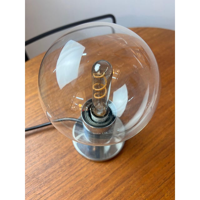 This table lamp consists of a chrome base and a transparent glass globe shade that screws onto the base. Inside, we have...