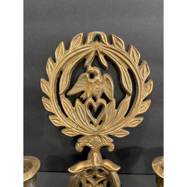 A pair of brass hanging sconces, each with an eagle, laurel and heart back plate issuing a two arm candle holder....