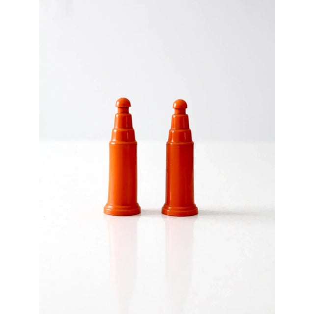 Vibrant vintage push-top salt and pepper shakers in bright orange plastic with a modern, streamlined silhouette. The...