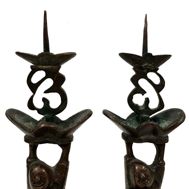 These early 20th century candlesticks are cast of bronze in the form of two Happy Buddhas standing on rectangle pedestal...