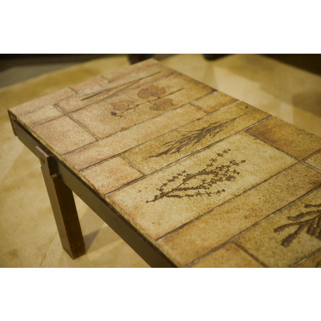 A rectangular coffee table from the 1960s, with a top made of sand-toned ceramic tiles. The "Herbier" design features...