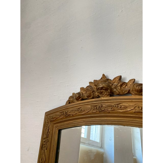 Rectangular giltwood mirror topped with a curved pediment carved in relief. The pediment features a bouquet of flowers and...