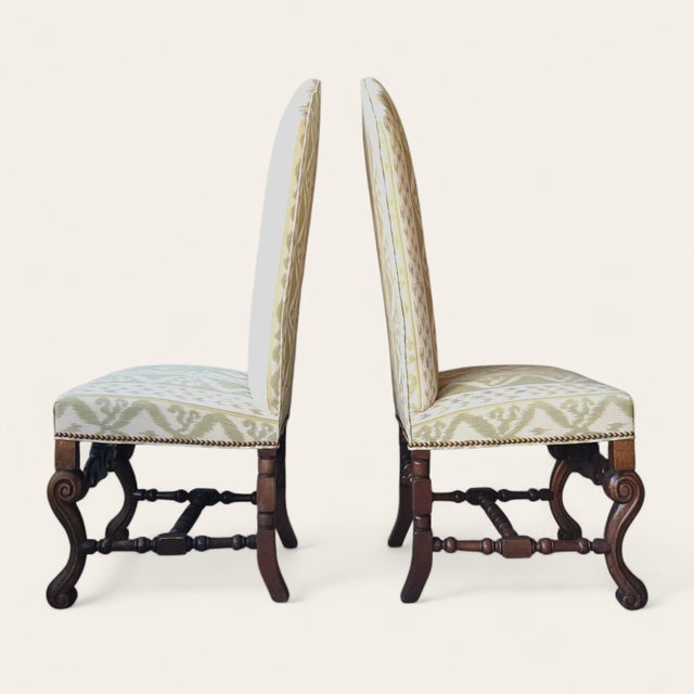 A pair of early–mid 20th century Flemish-style walnut side chairs featuring tall arched backs, robust carved bases, and...
