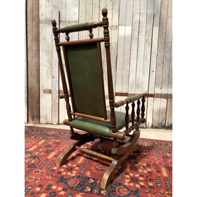 A stylish vintage rocking chair with a high backrest and elegant dark green leather upholstery. The deep green tone gives...