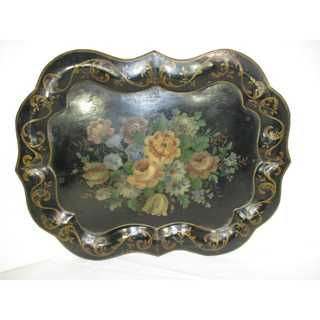 An antique hand-painted Victorian tole scalloped tray. It is painted black and decorated with a muted floral center in...