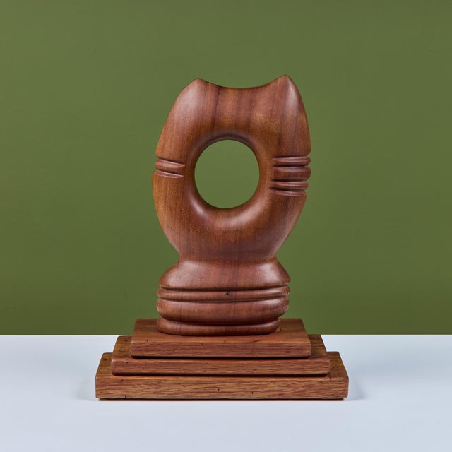 Hand-carved wooden abstract cat head. The piece showcases two pointed ears and whiskers on each side of the face. The...