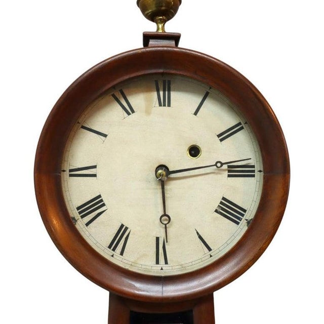 An American Federal style banjo clock, crafted from mahogany circa 1860. The clock features the classic form with a...