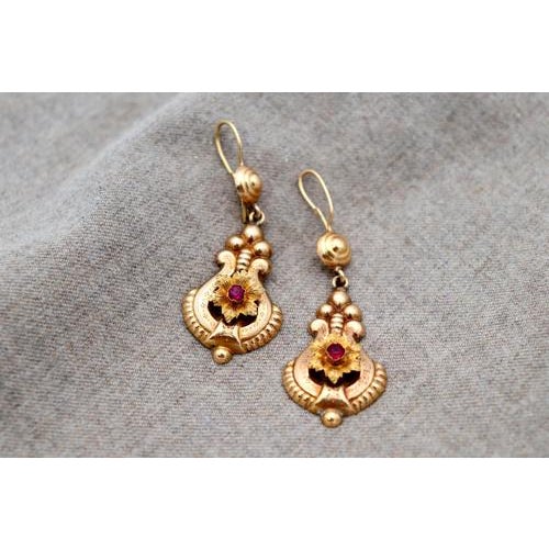 Gold earrings with reliefs and flower-shaped applications with synthetic garnet stones on a tilting pendant. Metal: Gold....