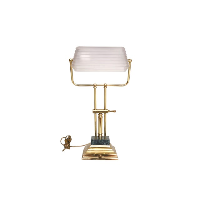 A brass, glass, and marble banker's desk lamp. A white beveled frosted glass shade is supported on a sleek brass support...