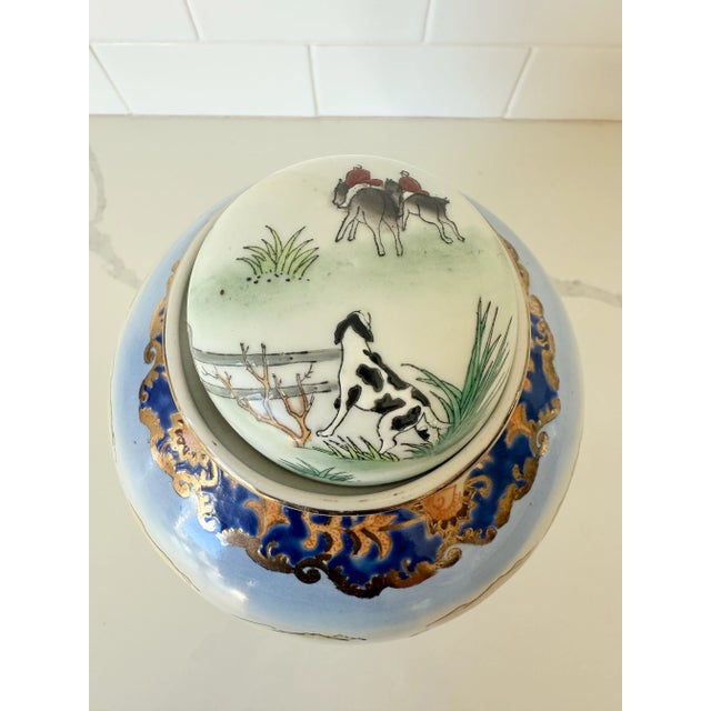A striking hand-painted lidded jar featuring an equestrian hunting scene, accented with fine detailing and vibrant colors....