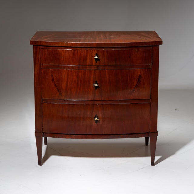 Three-drawer Biedermeier commode standing on square-tapered legs. The slightly convex front gives the piece a refined...