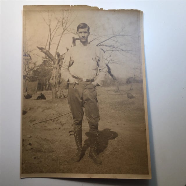 Sepia-toned antique photograph of what could be a farmer in high leather boots. He's surrounded by what appear to be...